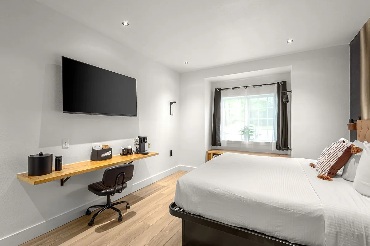 Boutique King Suite – room view with wall-mounted desk, chair, TV, and curtained window